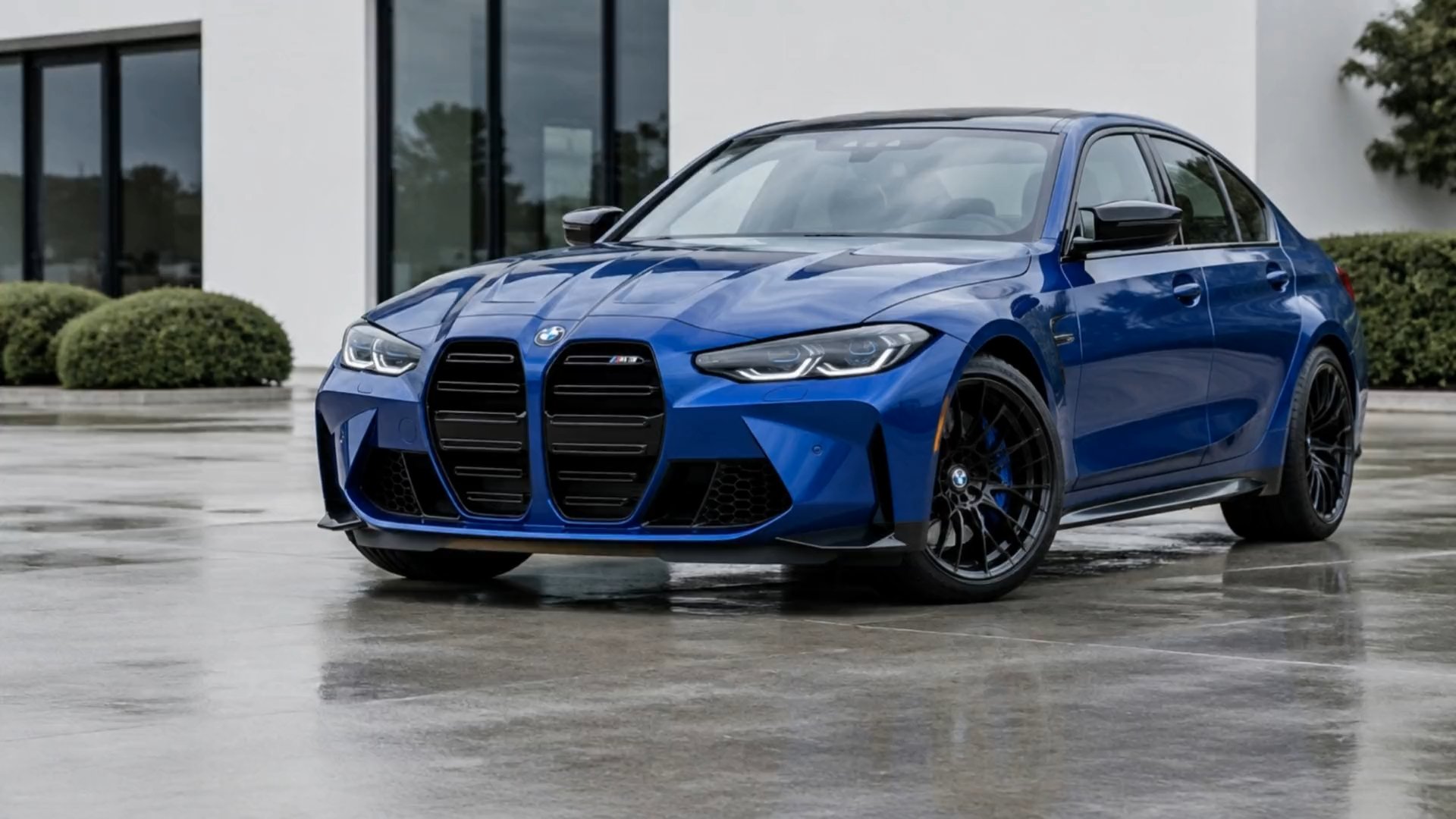 Blauwe BMW M3 vol schuim op lichtgrijs beton voor een wit gebouw